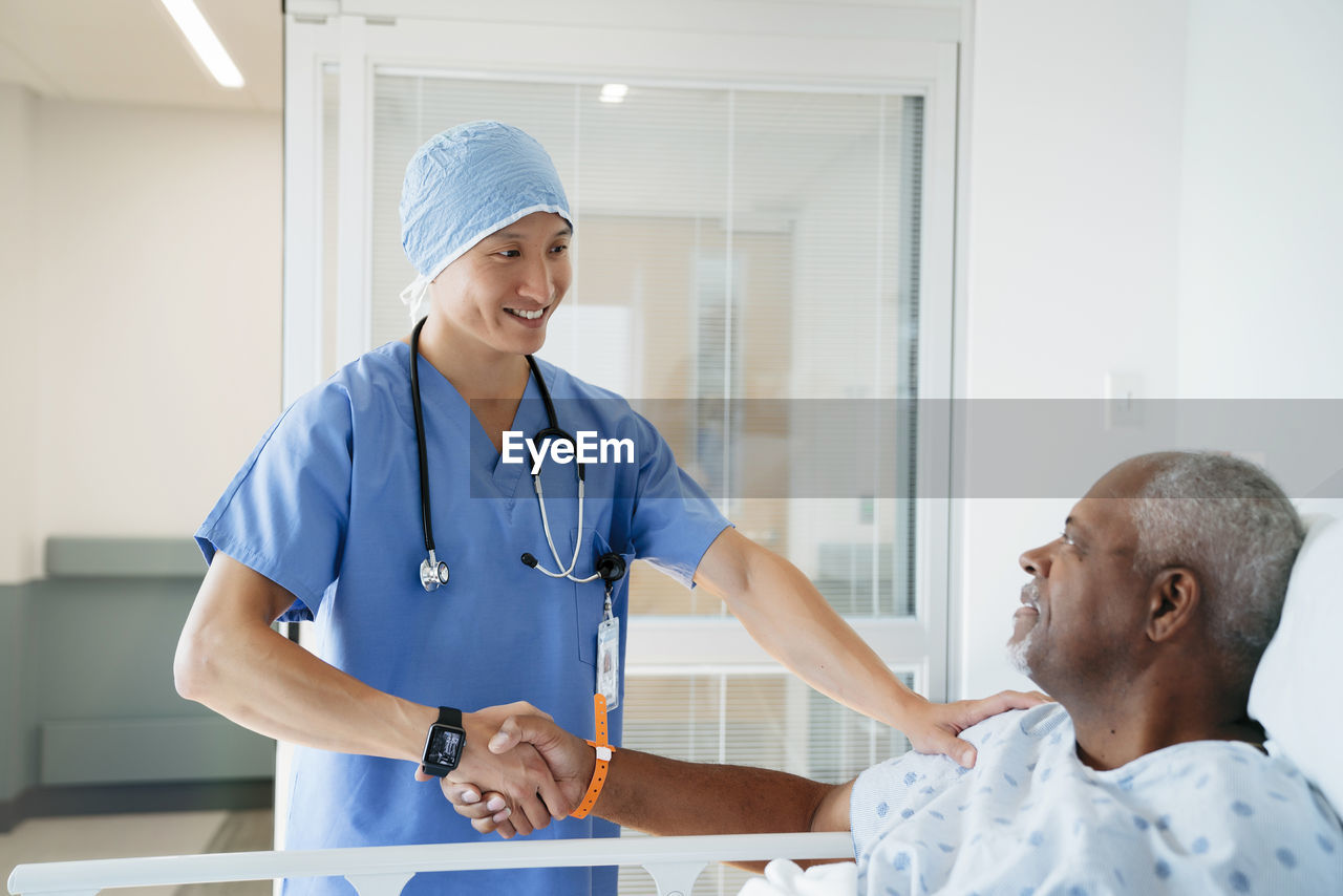 Confident surgeon shaking hands with senior patient in hospital ward