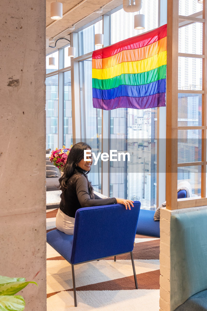 FULL LENGTH OF WOMAN SITTING ON MULTI COLORED CHAIR IN CAFE