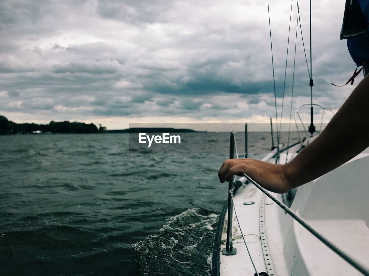 Cropped hand holding boat railing in sea against storm clouds