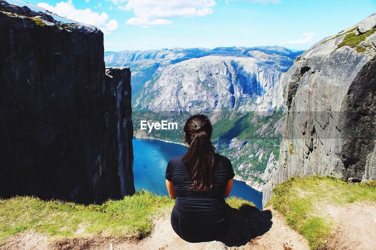 Rear view of woman sitting on cliff against mountains