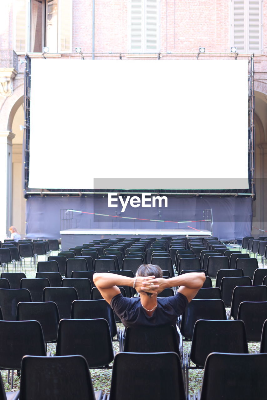 Rear view of man sitting against projection screen on chair