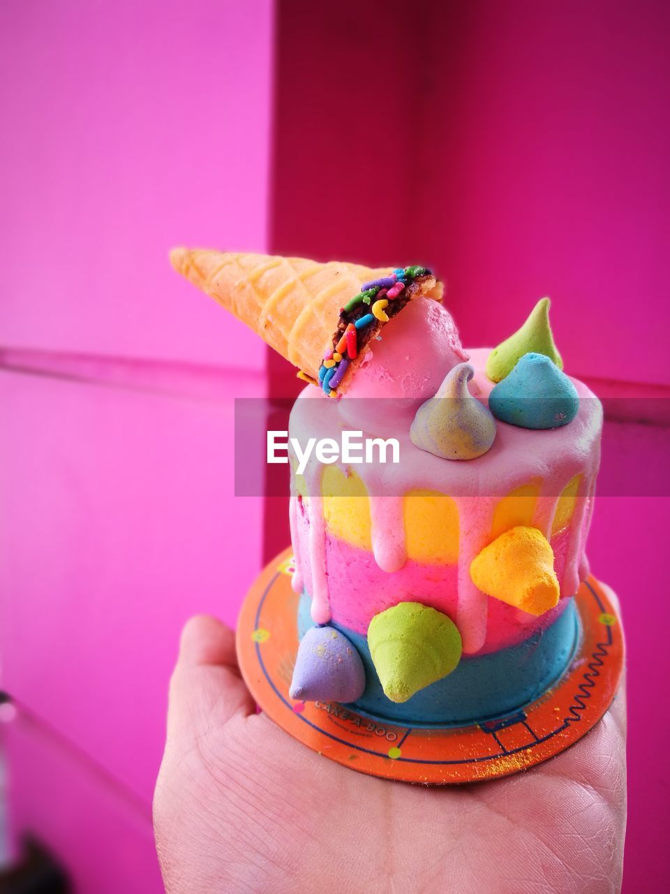 Cropped hand holding cake against pink wall