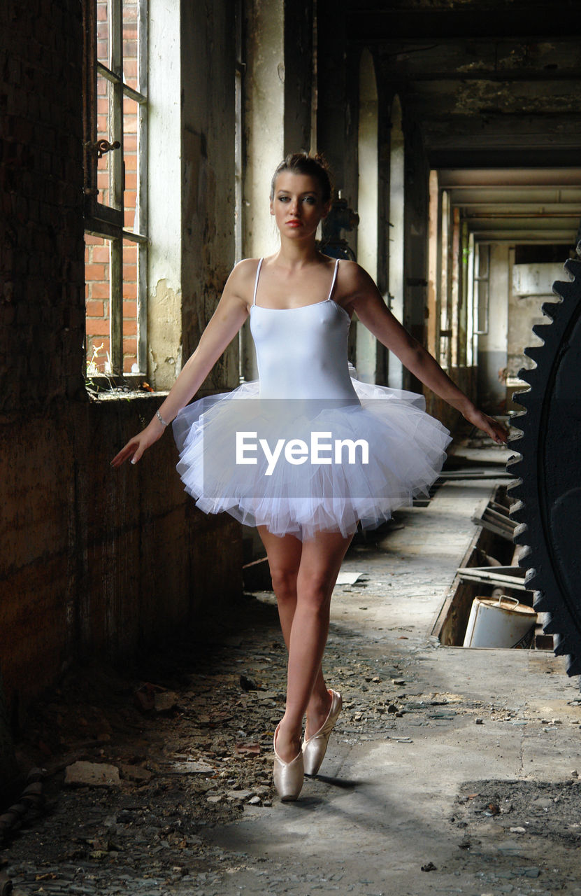 Full length portrait of ballerina dancing in abandoned building