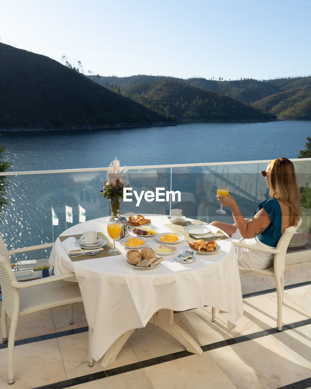 Woman sitting on table by lake against mountains