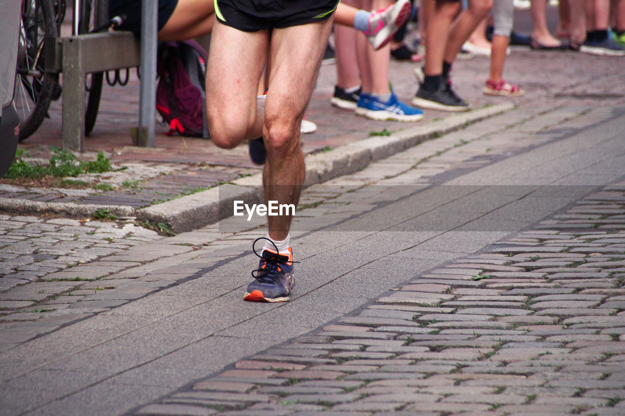 Low section of athlete running marathon on street with people in background