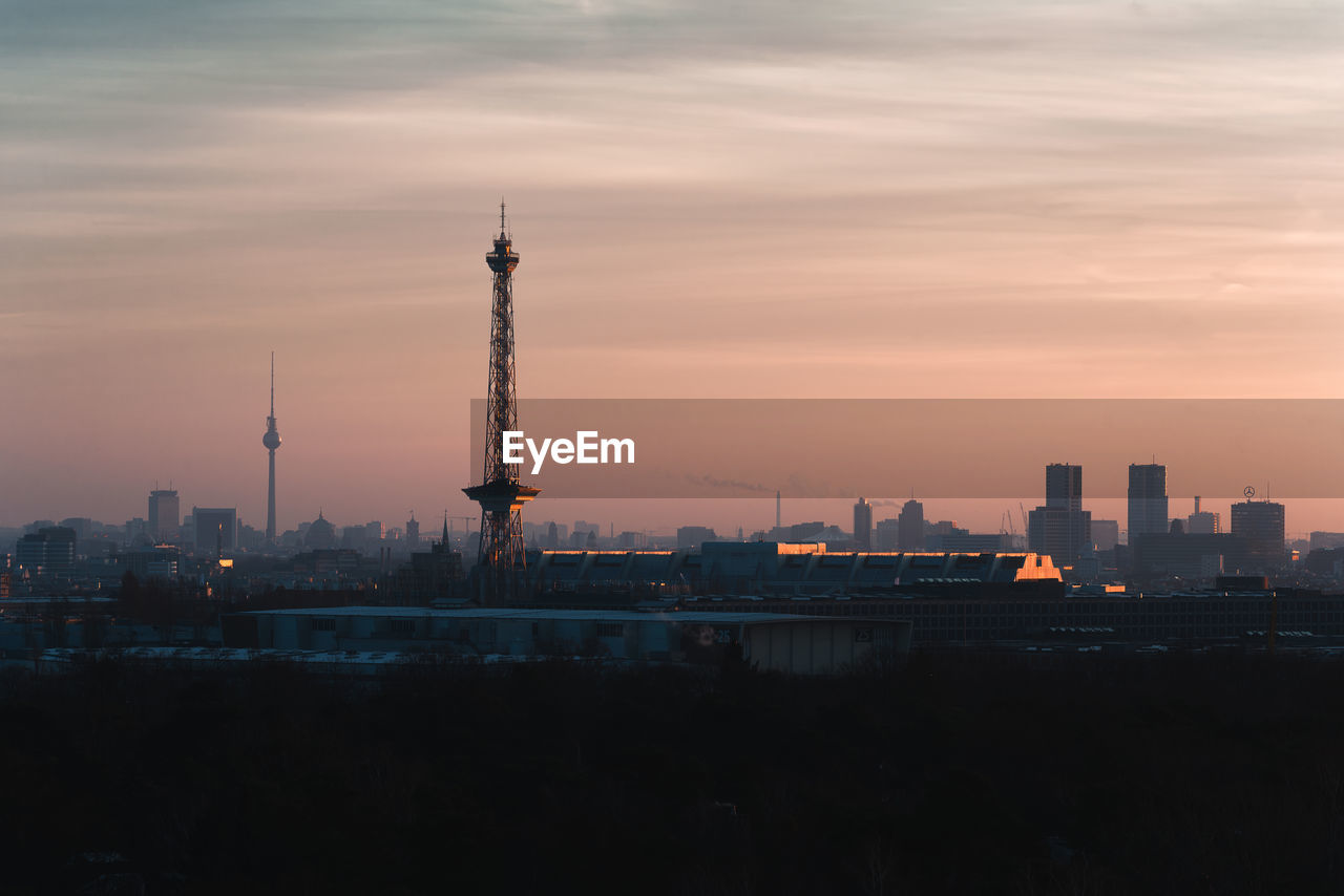 Communications tower in city against sky during sunset