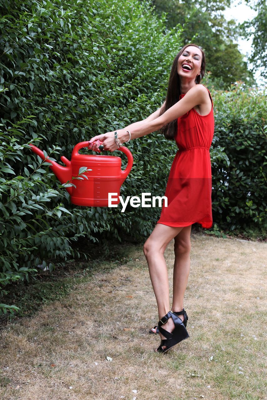 Portrait of smiling woman watering plants in yard