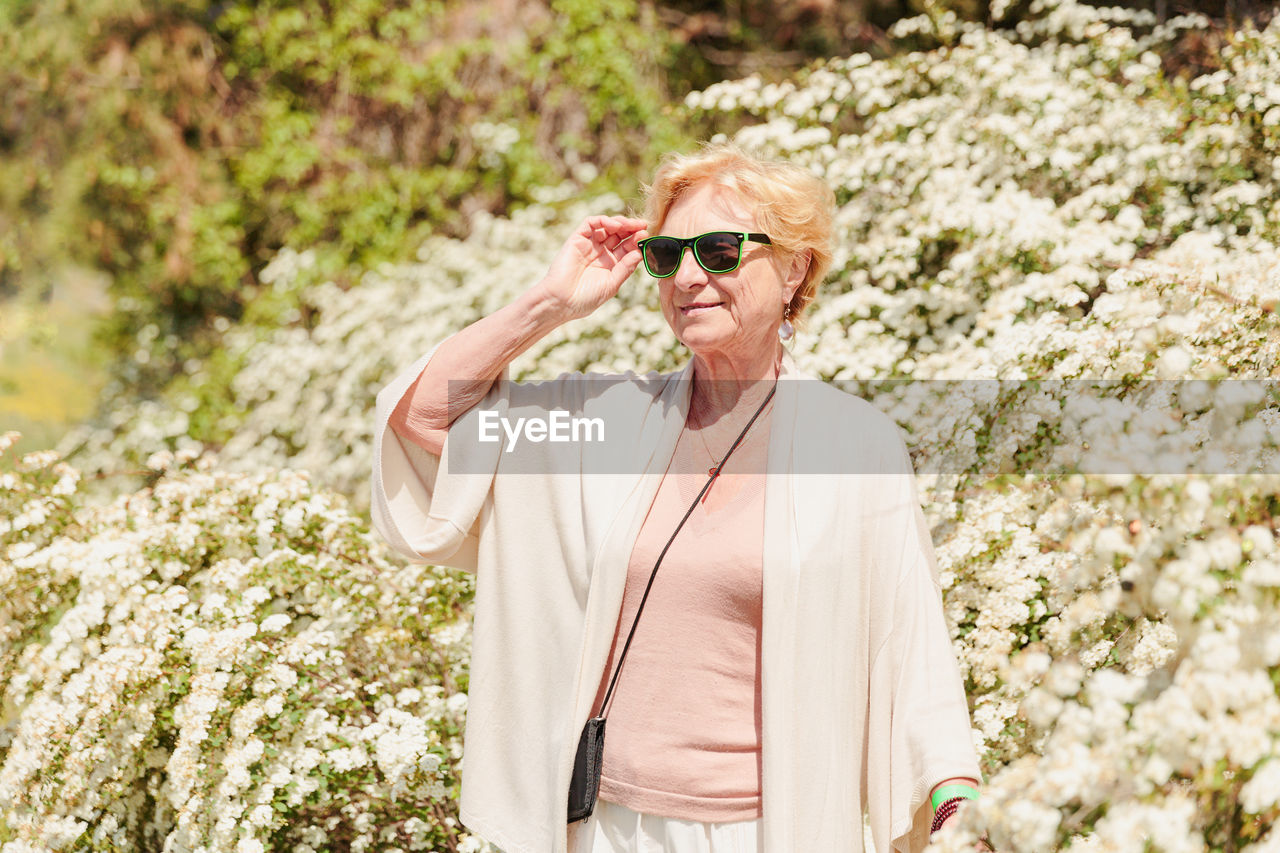 Elderly woman posing among bushes with white flowers