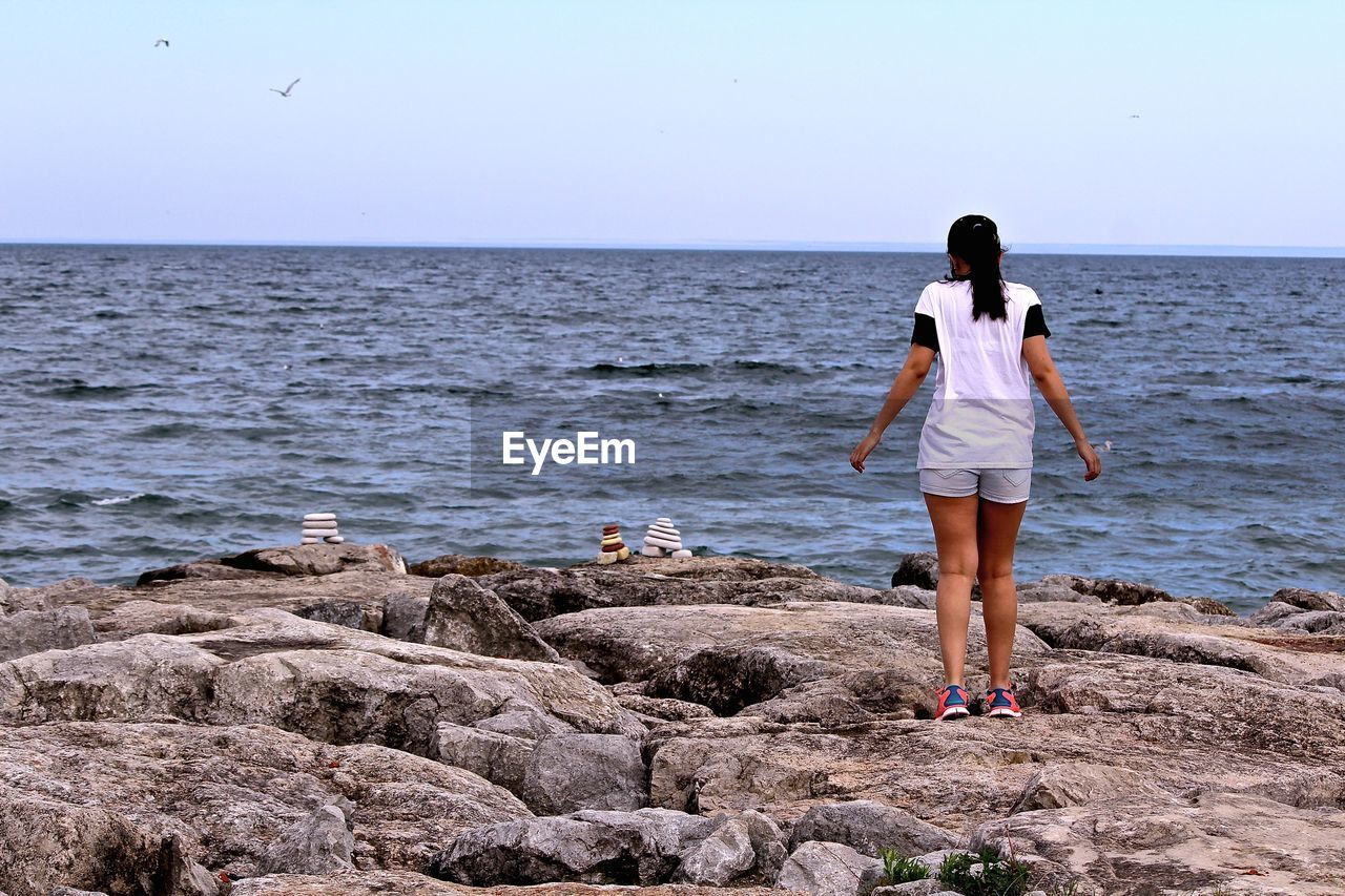 Rear view of woman standing on beach against clear sky