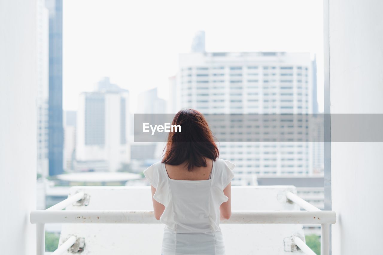 Rear view of woman standing by window in city