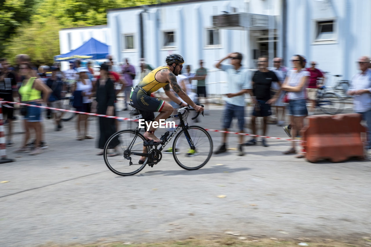bicycle, transportation, sports, motion, activity, city, architecture, cycling, endurance sports, group of people, street, blurred motion, men, mode of transportation, road cycling, cycle sport, vehicle, bicycle racing, lifestyles, crowd, city life, adult, large group of people, building exterior, city street, riding, built structure, road bicycle racing, race, wheel, women, on the move, speed, road bicycle, sports equipment, commuter, full length, land vehicle, road, day, racing bicycle, person, outdoors, leisure activity, travel, competition, recreation, bicycle wheel, clothing
