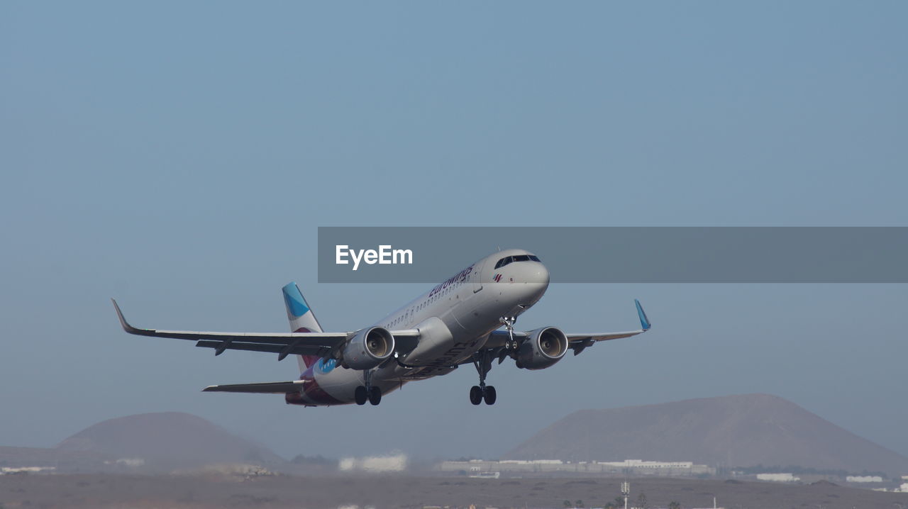 AIRPLANE FLYING OVER MOUNTAINS AGAINST SKY