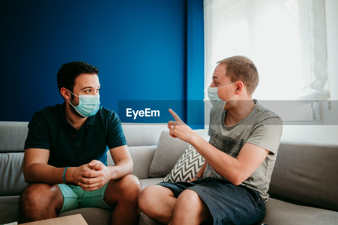 People wearing mask sitting on sofa at home