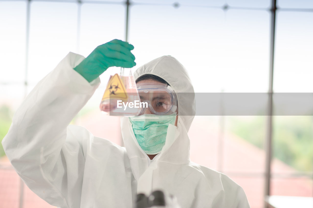 Scientist wearing protective suit holding flask at laboratory