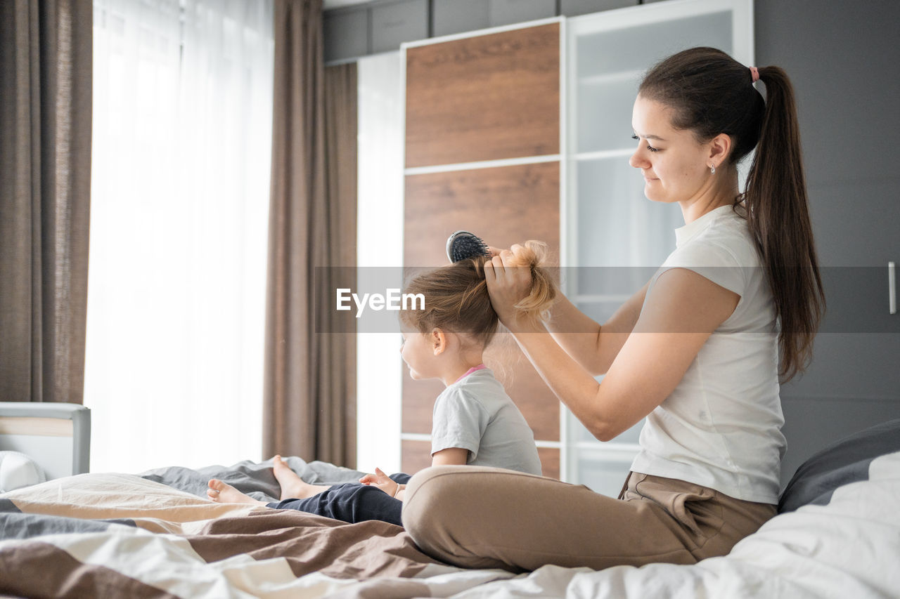 side view of young woman using mobile phone while lying on bed at home