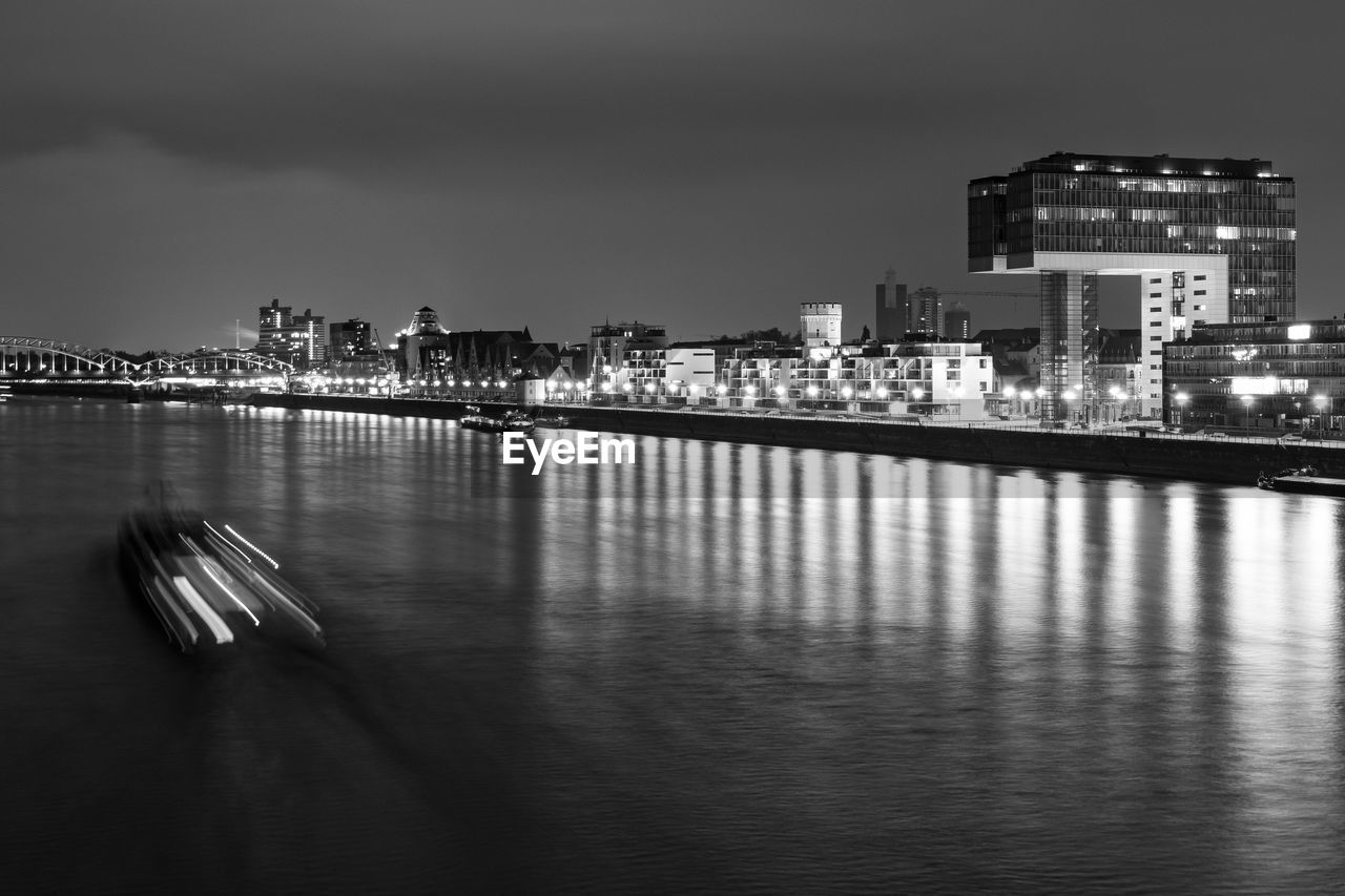 ILLUMINATED CITYSCAPE BY WATER AGAINST SKY