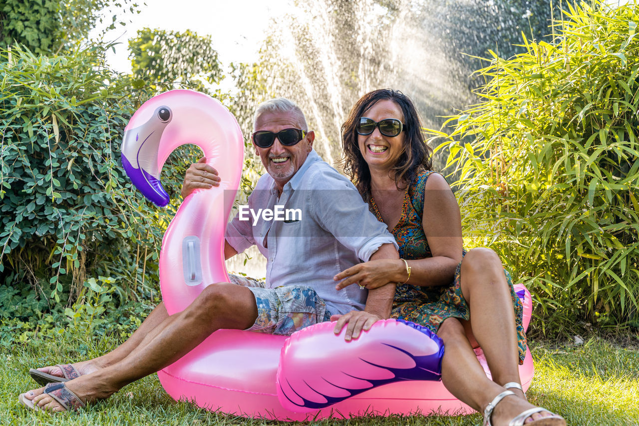 Beautiful smiling middle aged couple having fun sitting on pink flamingo inflatable toy