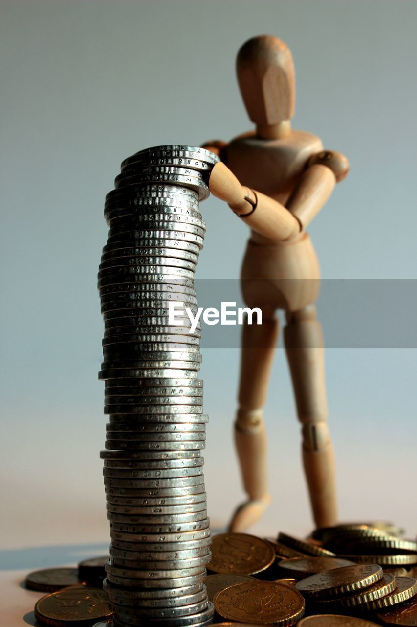 Close-up of figurine with stacked coins on white background