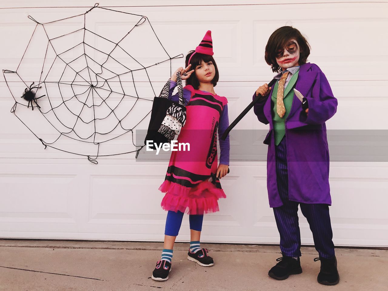 Full length of girl and boy in costume standing against wall