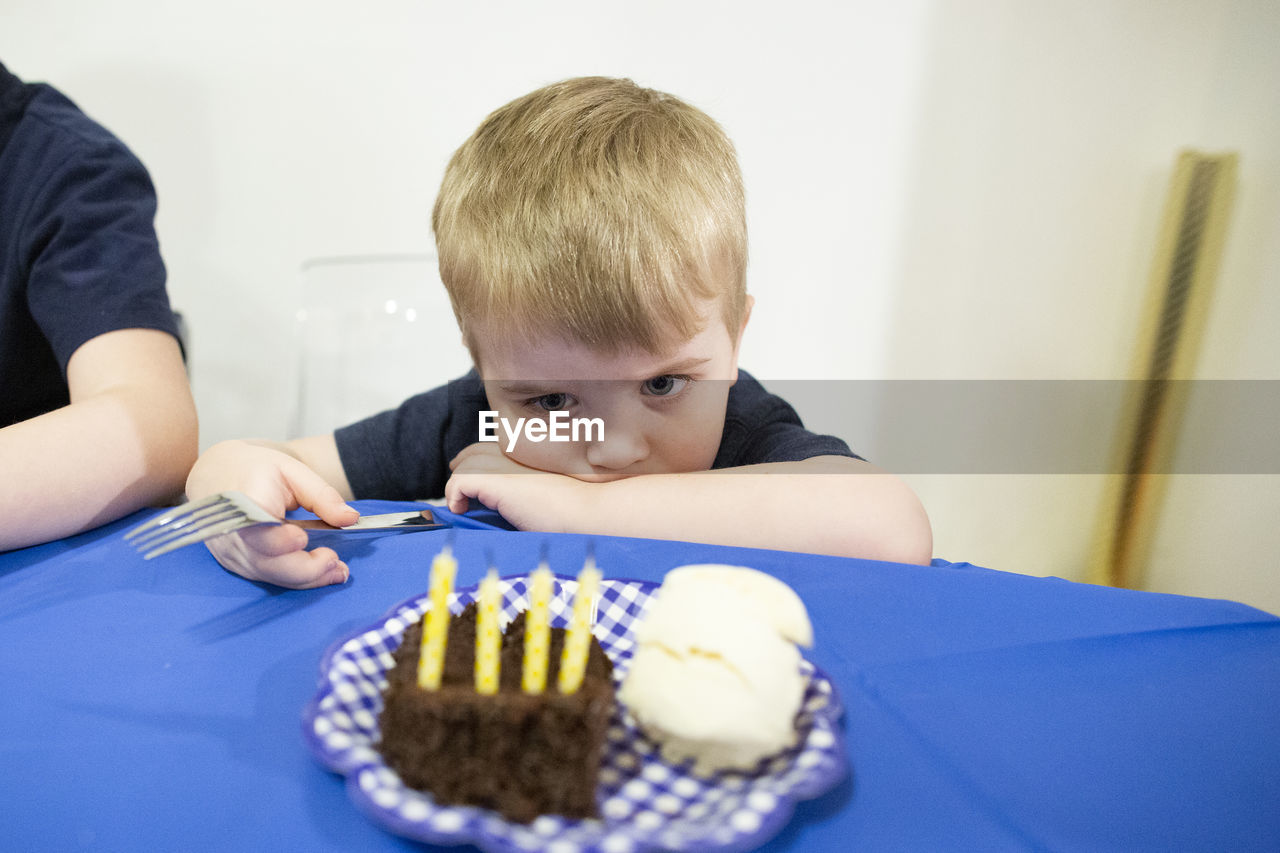 Child sits at table staring at birthday candles in piece of cake