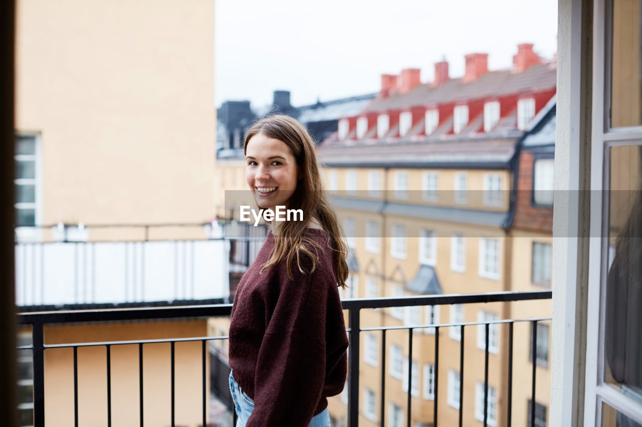 Side view of smiling woman standing in balcony at rental apartment