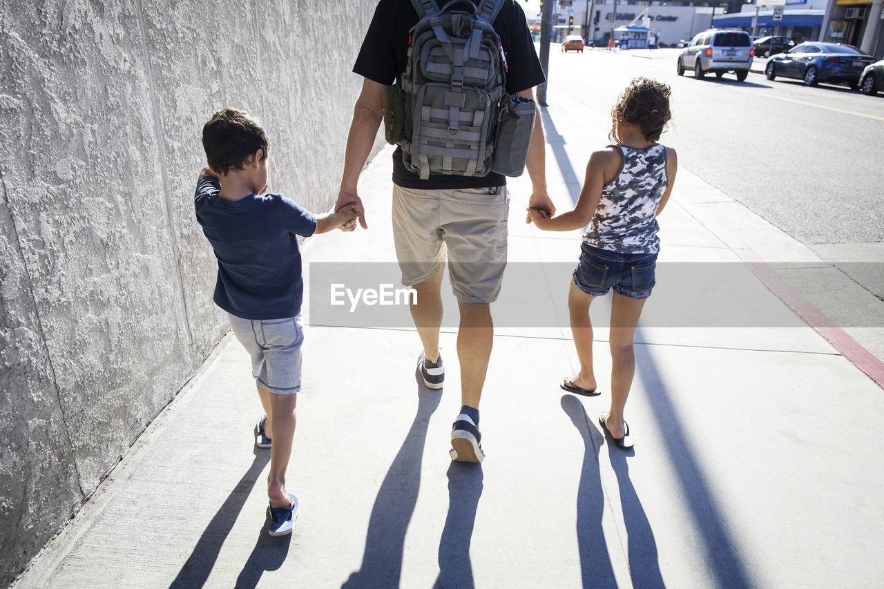 Rear view of father walking with children on sidewalk in city