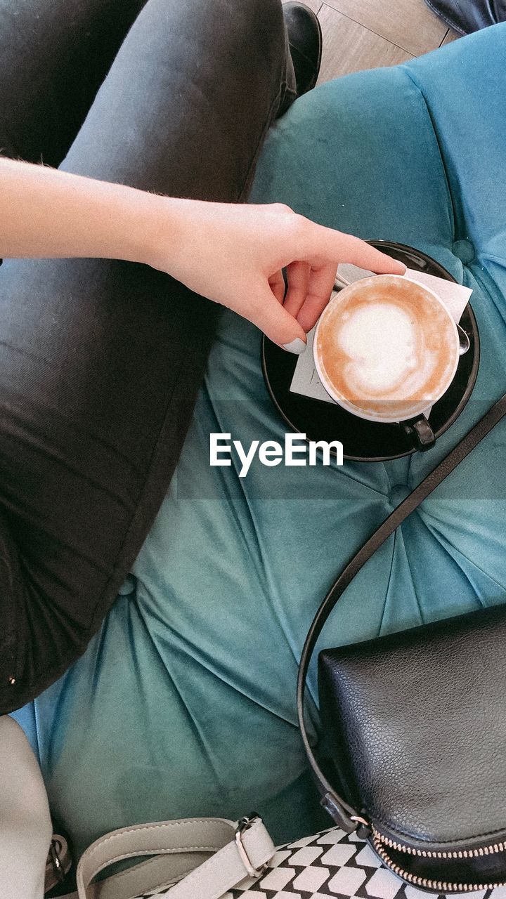 Low section of woman having coffee while sitting on sofa