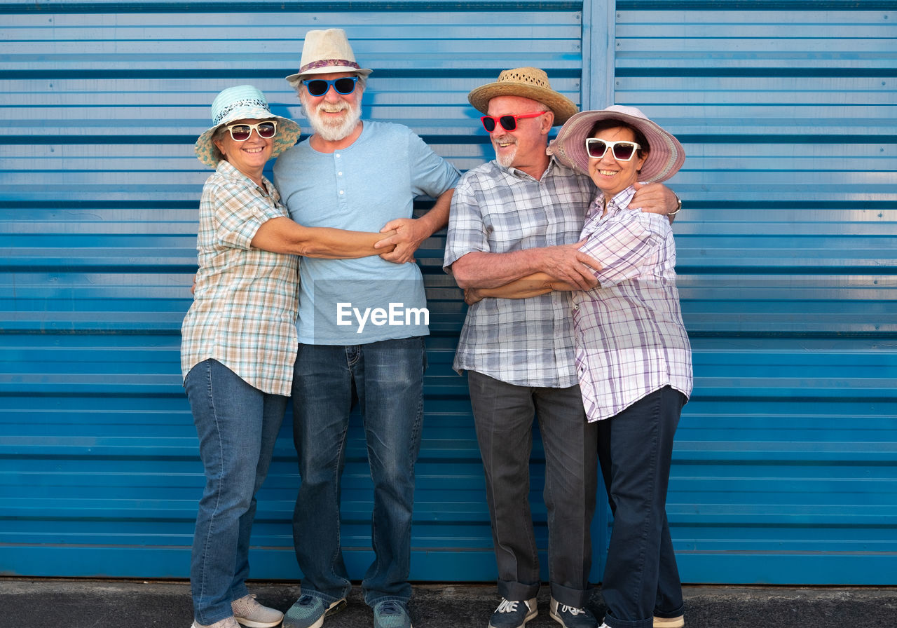 Portrait of smiling friends wearing sunglasses and hats against wall