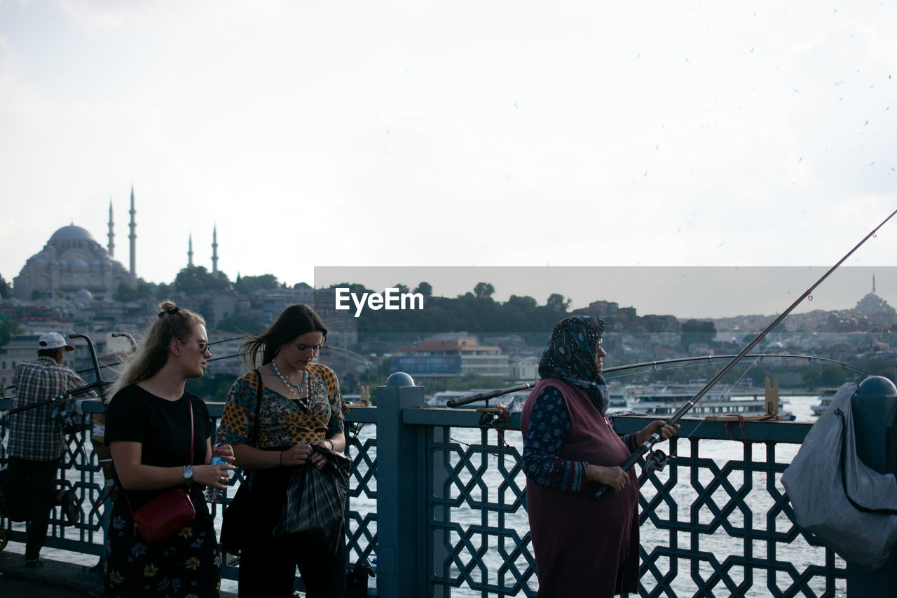 PEOPLE STANDING ON RAILING AGAINST CLEAR SKY