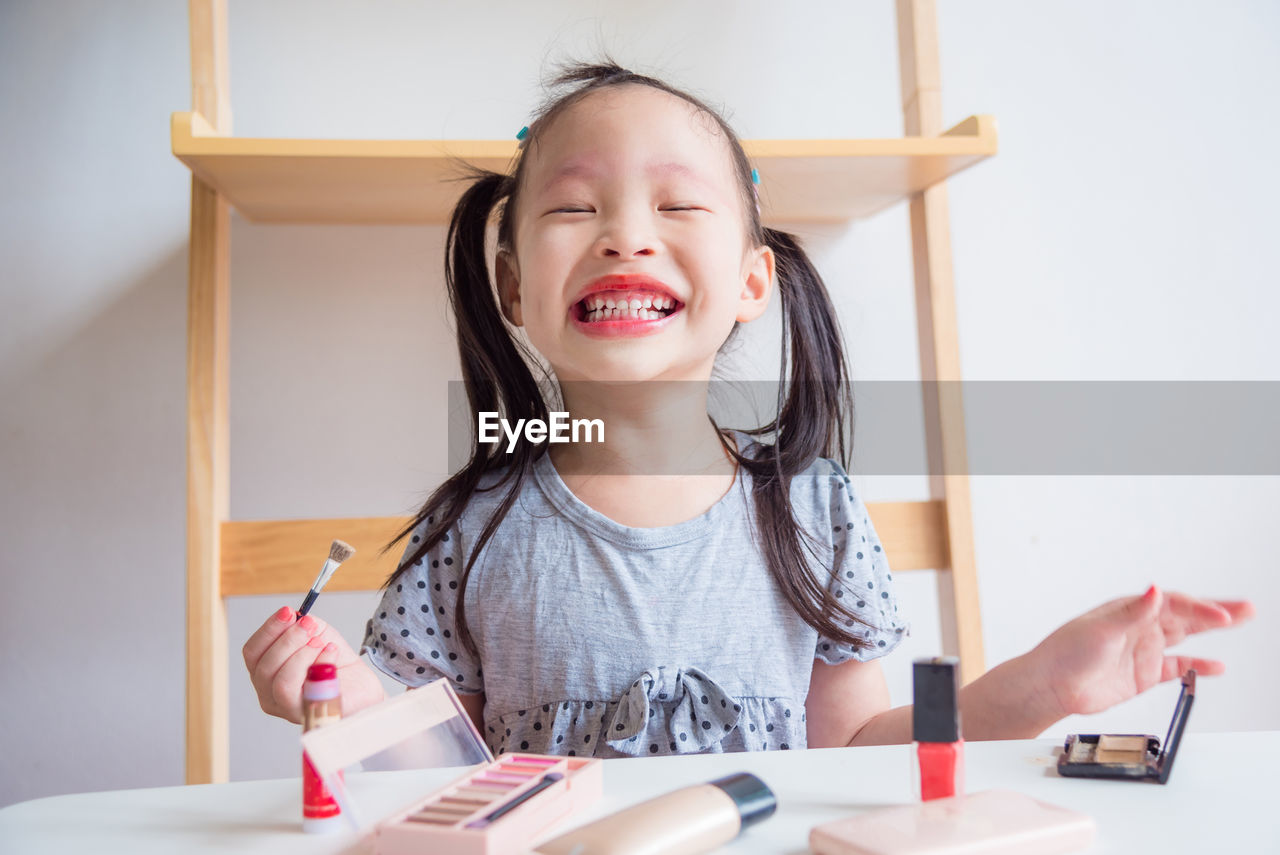 Smiling girl wearing lipstick while sitting at table in home