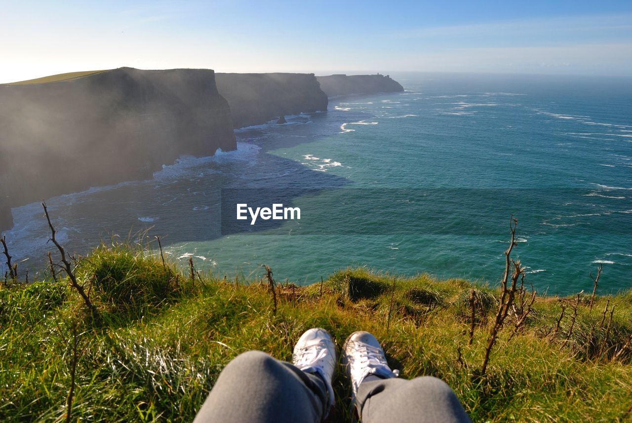 Low section of woman sitting on hill by sea against sky