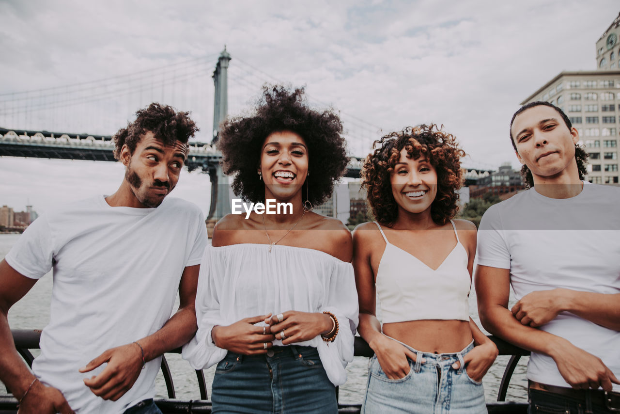 Cheerful friends standing against bridge in city