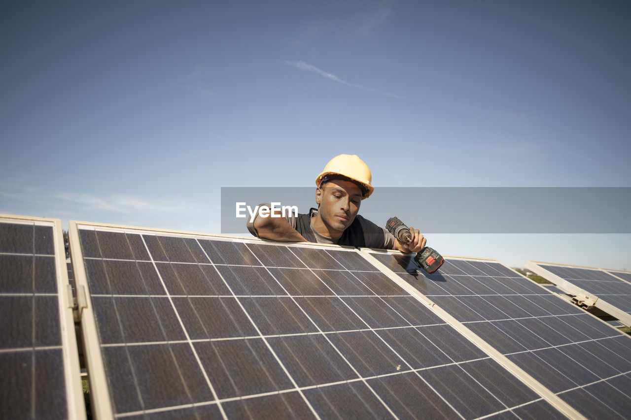 Young male engineer holding drill while examining solar panels at power station