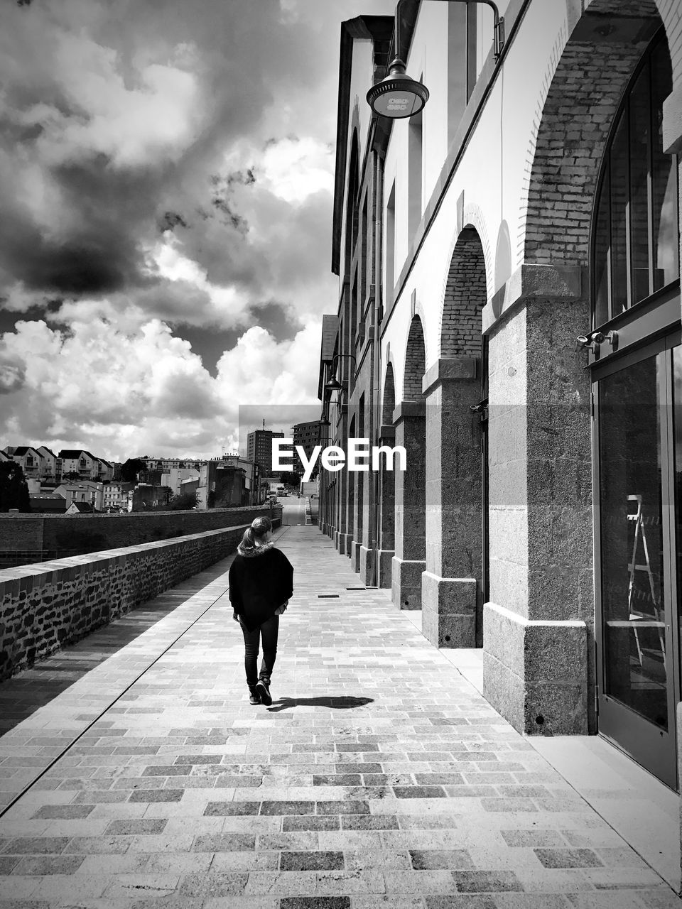 Rear view of woman walking by buildings on sidewalk