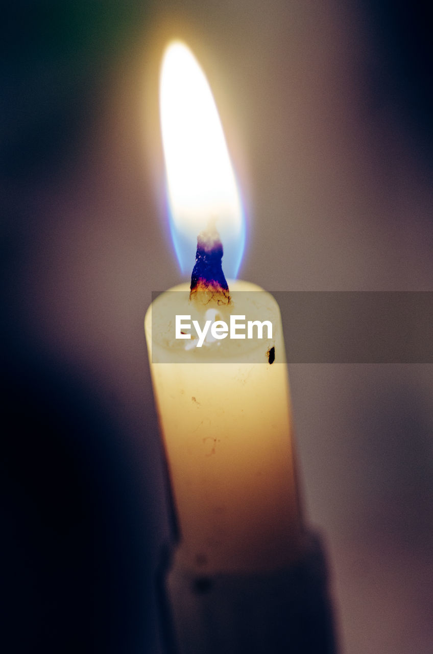 CLOSE-UP OF LIT CANDLE IN DARK ROOM