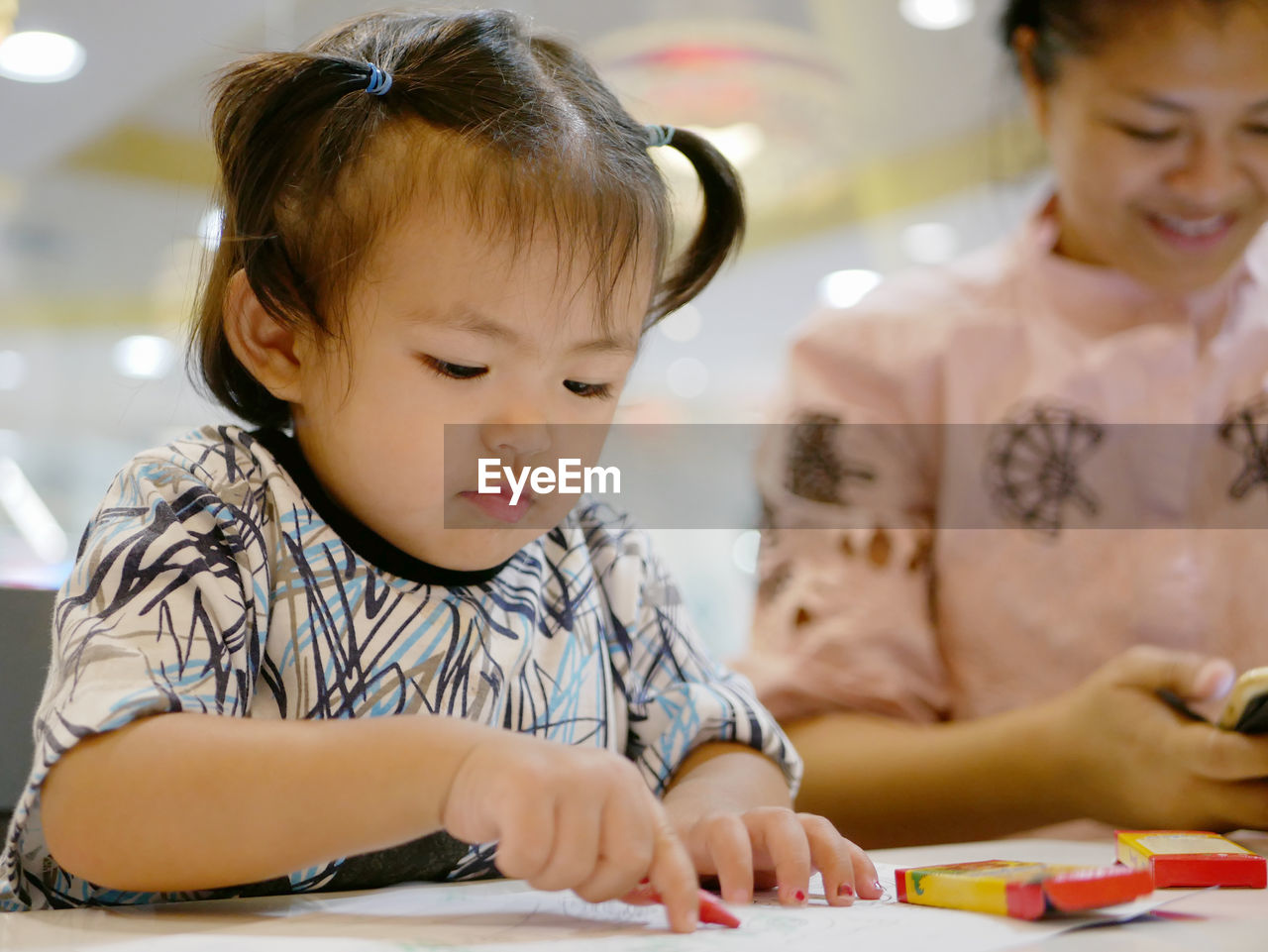 Cute baby girl coloring paper at table in restaurant