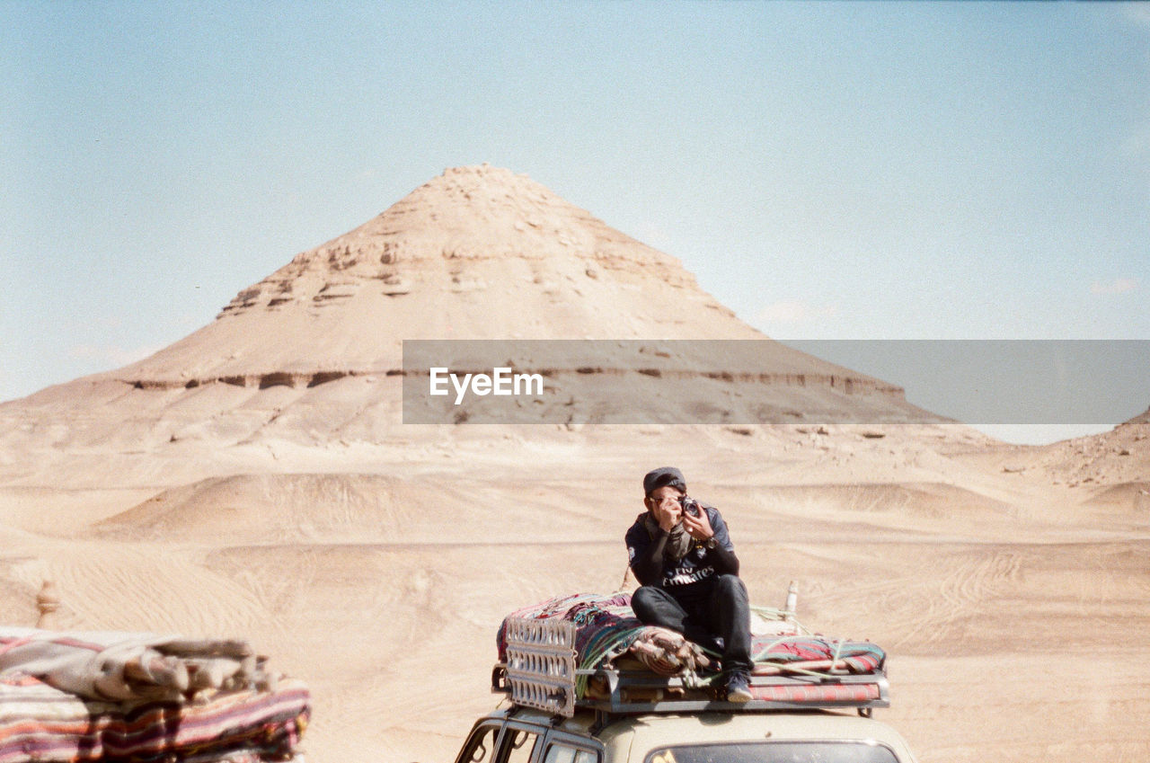 REAR VIEW OF WOMAN SITTING ON DESERT