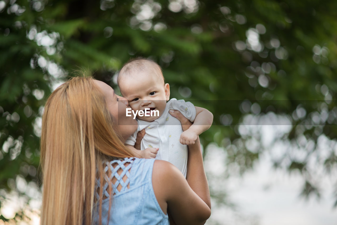 Close-up of mother kissing daughter against tree