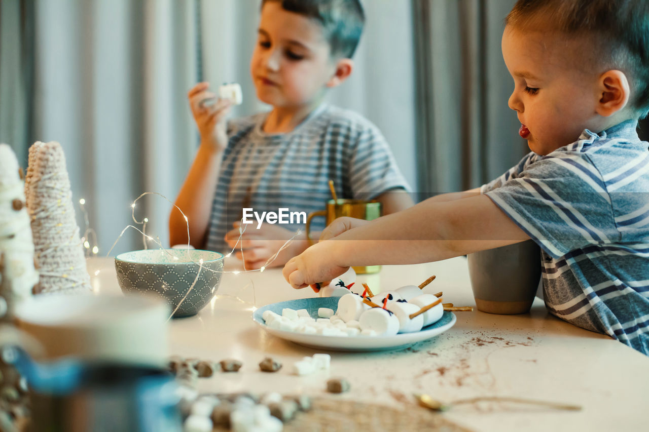 Cute brothers decorating marshmallows at home