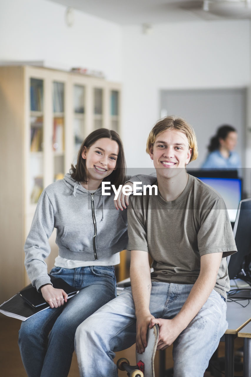 Portrait of smiling high school students sitting on desk in computer lab