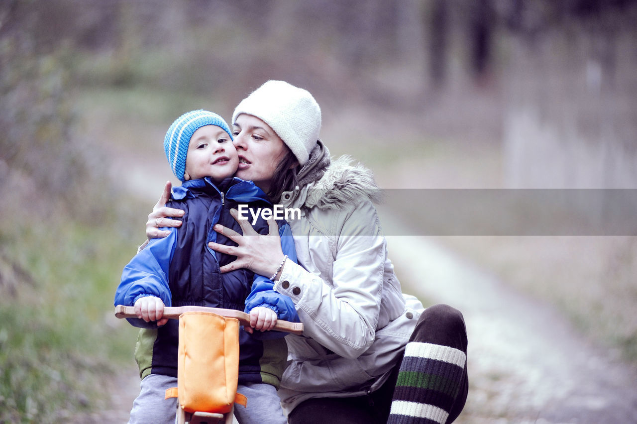 Mother kissing son riding bicycle at park during winter