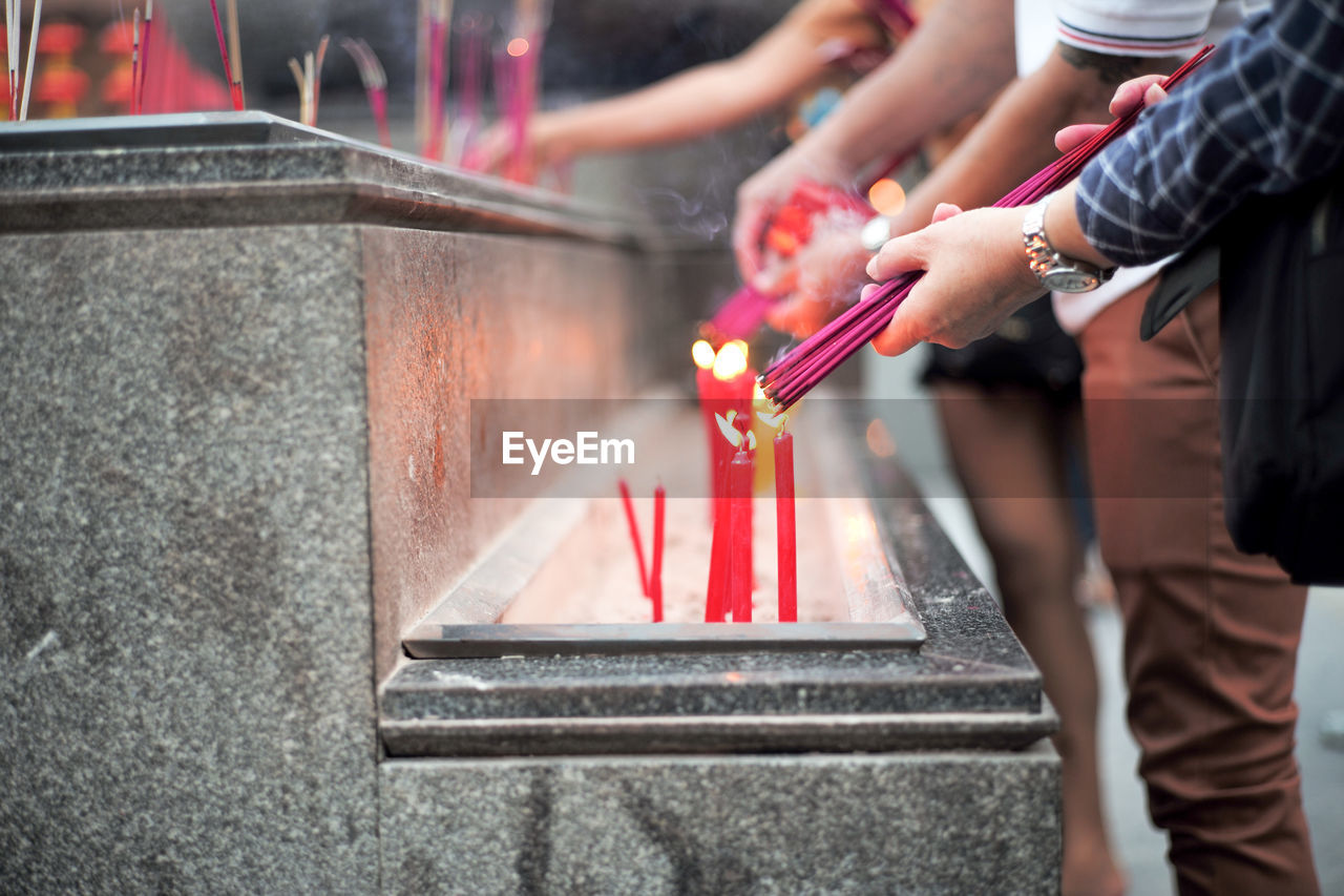 Closeup hands holding the bundle of incenses for lighting with candles in the sand tray