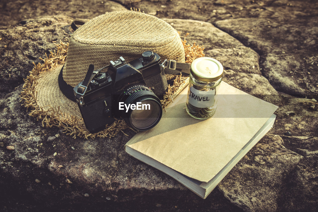 High angle view of camera with money and book by hat on rock formation