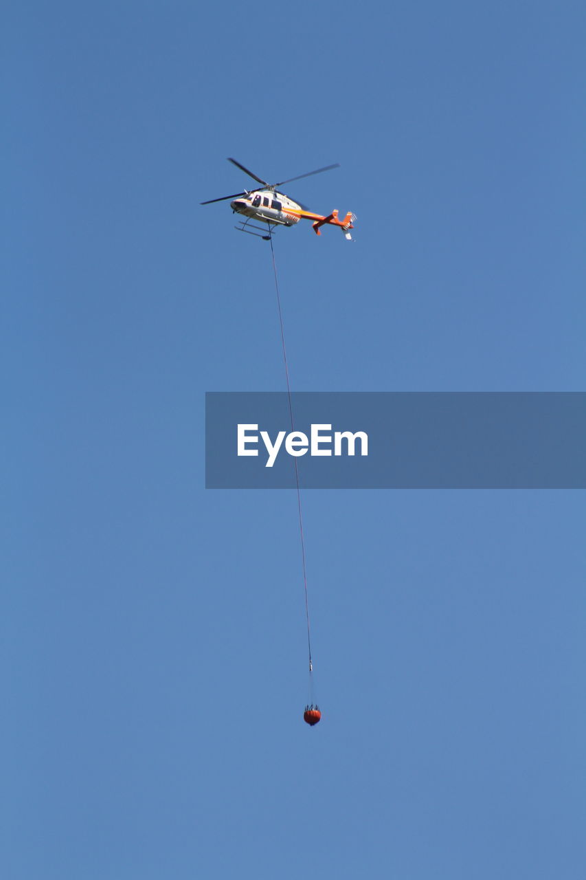 Low angle view of rope hanging from helicopter against clear blue sky