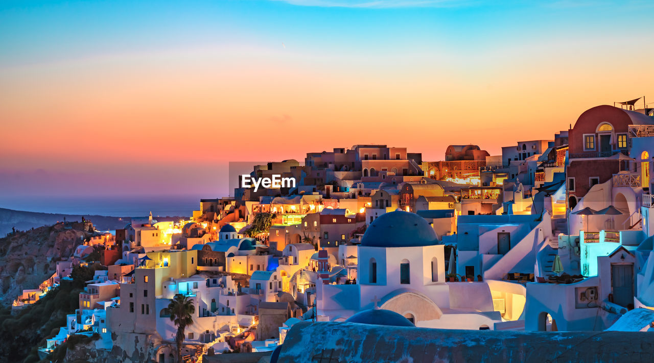 Illuminated buildings in town against orange sky