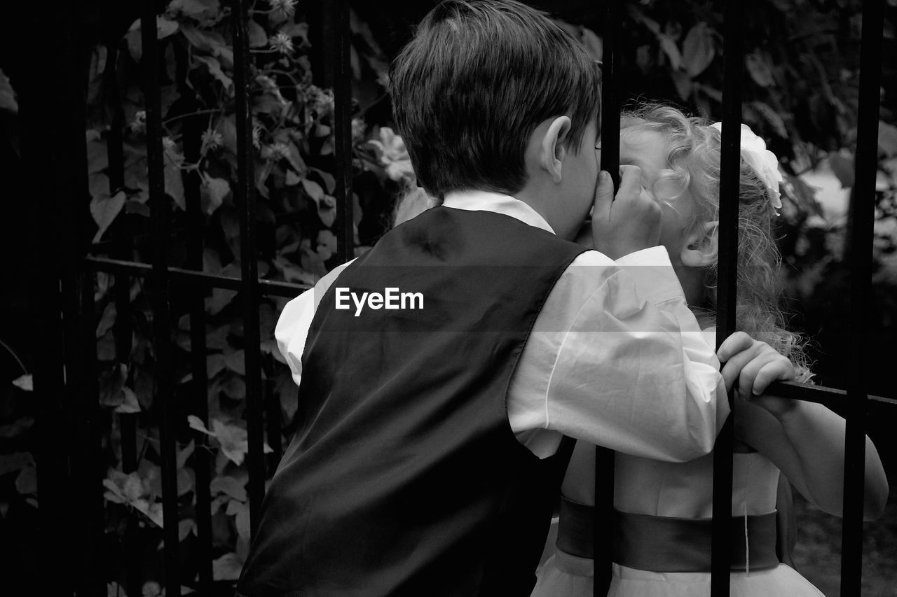 Adorable children kissing through metal fence