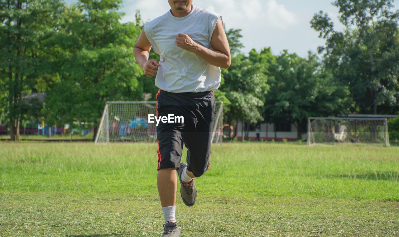 Low section of man running on grassy field at park