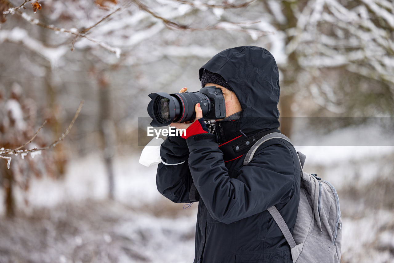 Woman with professional camera equipment taking a photo in winter forest, germany