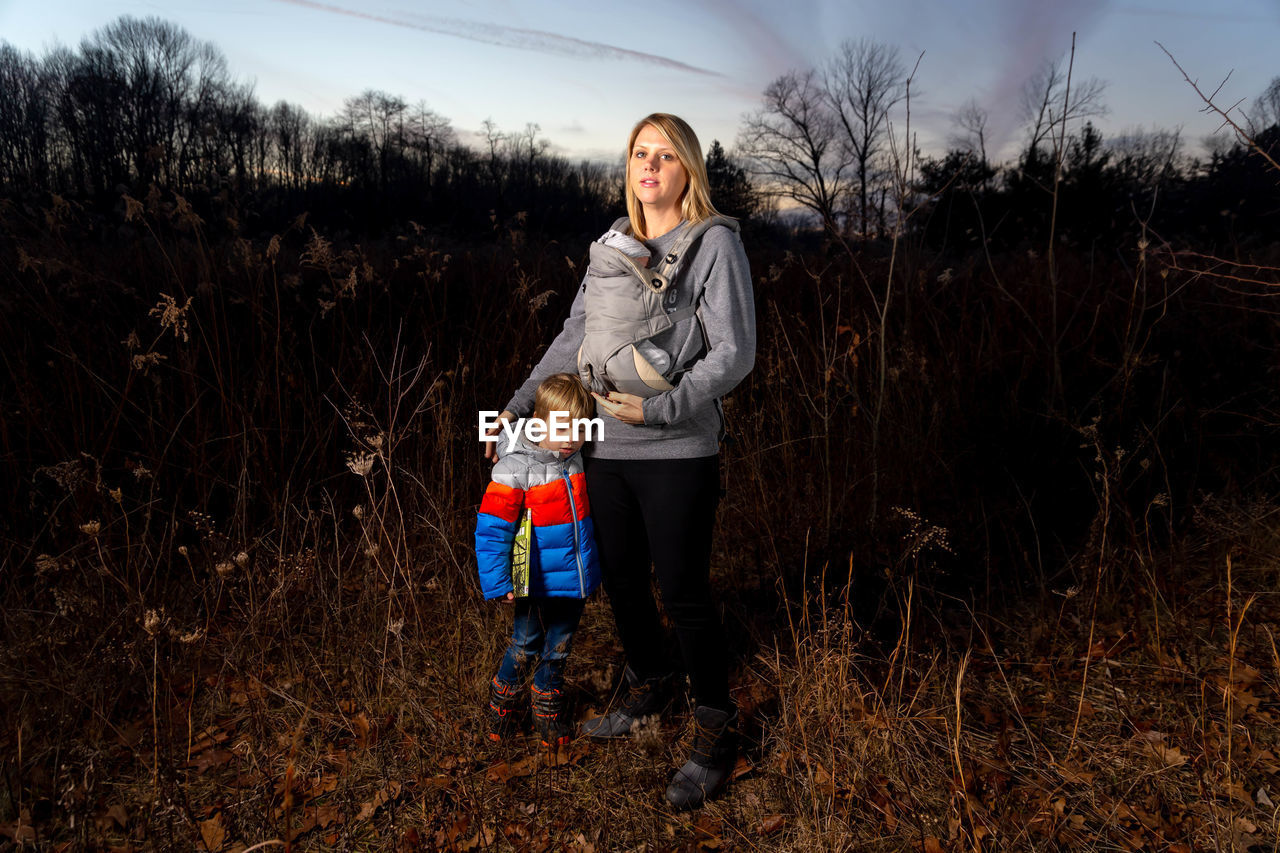 SIBLINGS STANDING ON FIELD AGAINST SKY