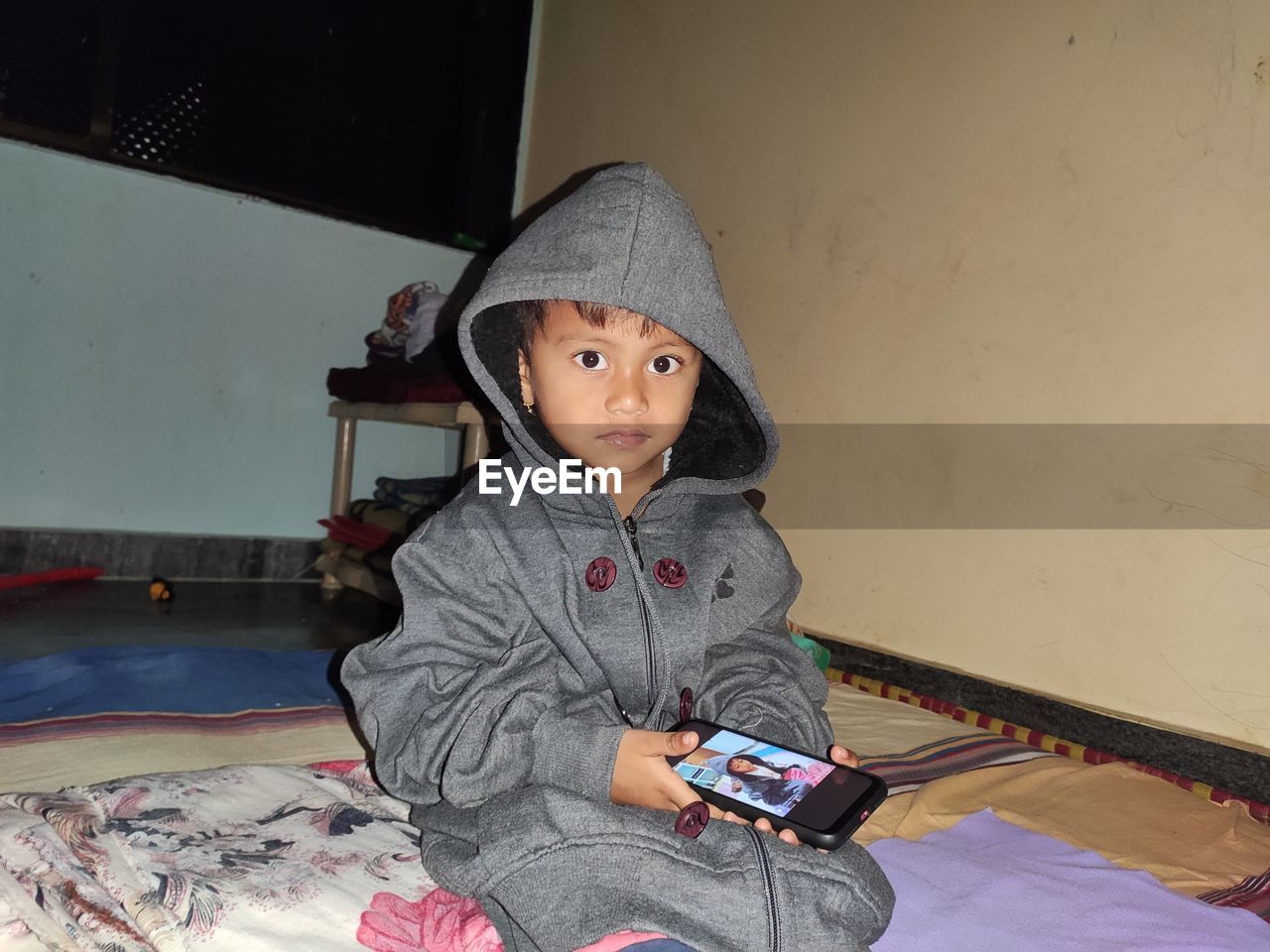 PORTRAIT OF CUTE BOY USING MOBILE PHONE WHILE RELAXING ON BED AT HOME